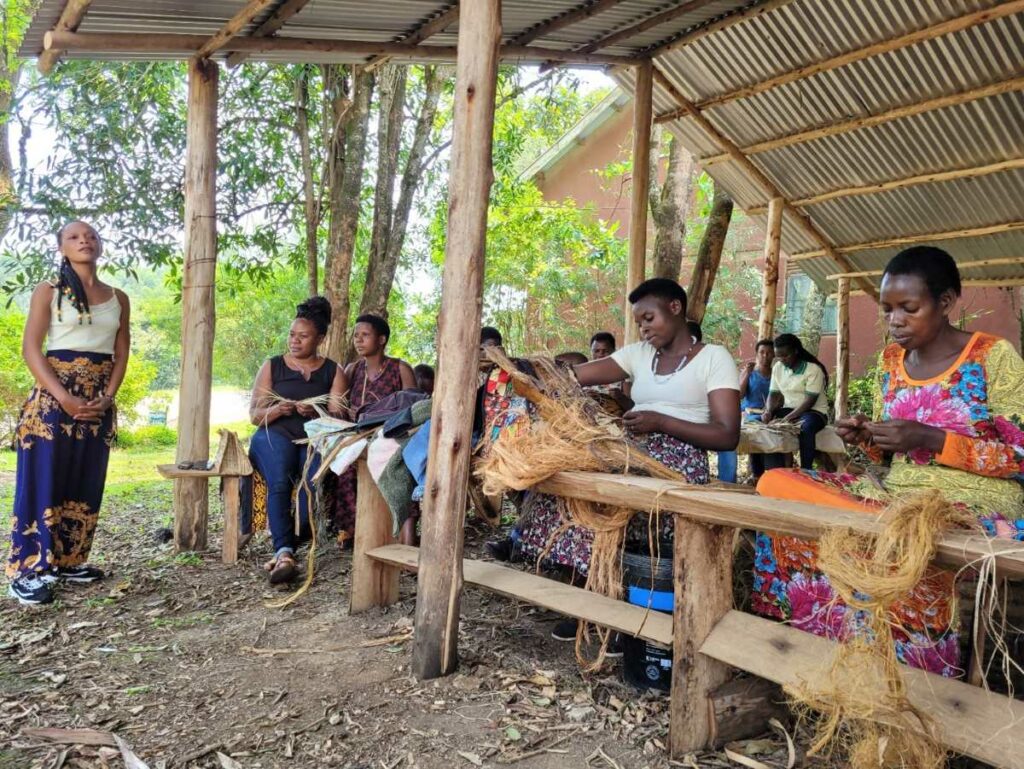 Frauen aus Bigodi sitzen zusammen und stellen individuell gestaltete Taschen und Matten aus Sumpfgras her