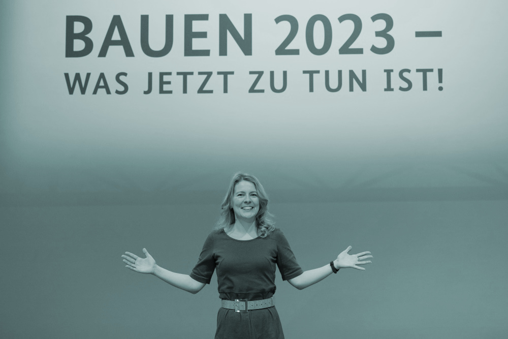 Tina Teucher Moderatorin auf Messe BAU 2023; Text auf Hintergrund: BAUEN 2023 - Was jetzt zu tun ist!