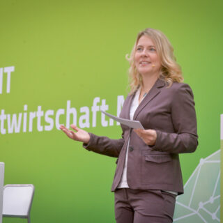 Tina Teucher moderiert vor einer grünen Leinwand