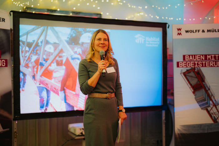 Tina Teucher moderiert vor einem großen Bildschirm